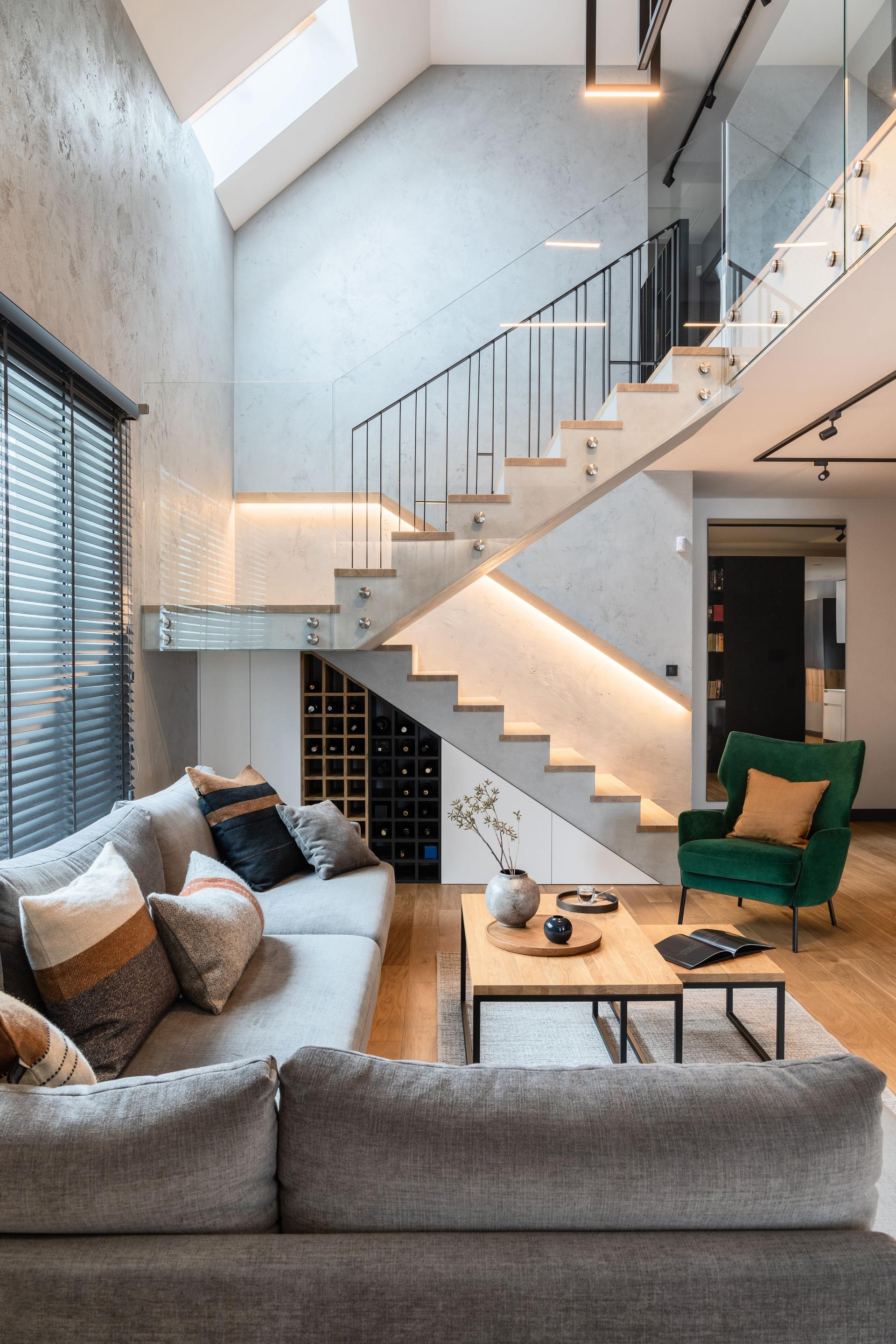 Stylish composition of stairs in living room interior. Grey sofa, green velvet armchair, coffee table and minimalist personal accessories. Modern home decor. Template.
